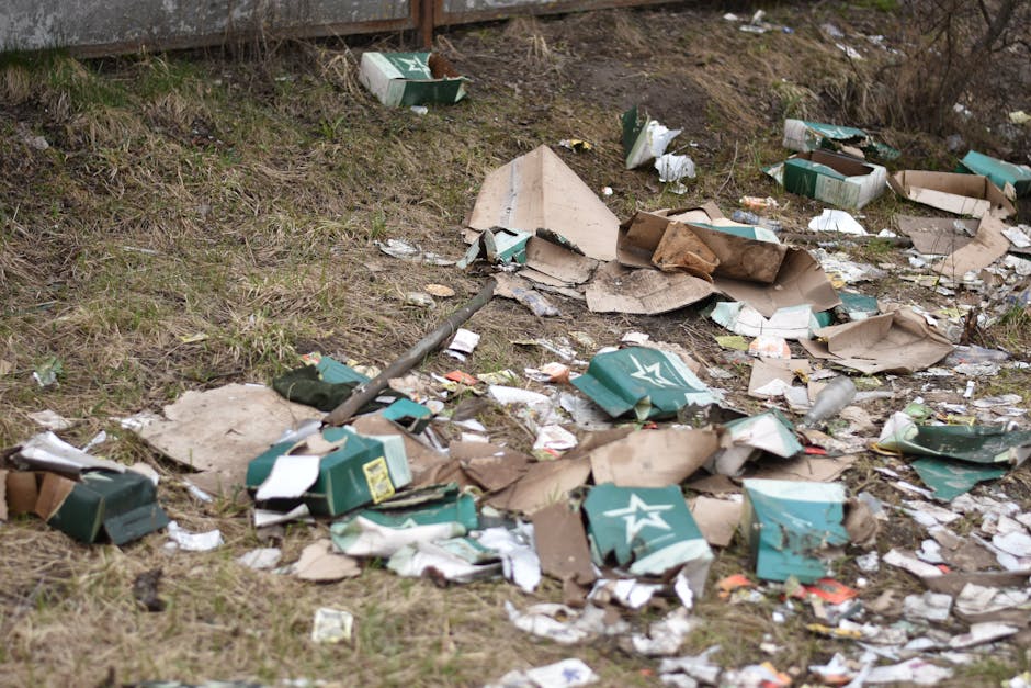 A pile of mixed domestic rubbish is scattered across a hard surface, consisting of various discarded items including plastic bottles, food containers, crumpled paper, and packaging materials. The plastic bottles are transparent with labels and caps, some appearing partially crushed or squeezed. There are crumpled tissue papers, paper bags, and cardboard packaging, all showing signs of wear and folding. The background reveals more waste items, including boxes and loose debris, creating a cluttered scene typical of unmanaged household refuse. The surface beneath the rubbish appears to be an outdoor driveway or pavement, with no visible waste bin or collection vehicle in the vicinity. The overall scene is devoid of any recycling or disposal machinery, emphasizing the need for effective rubbish removal services such as those provided by House Clearance Dulwich for private waste handling or alternative collection options, matching the context of rubbish collection timing and access issues for Dulwich homes.
